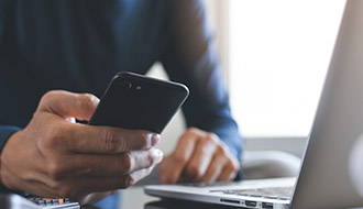 hand holding a phone next to a laptop