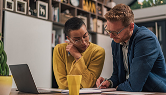 two people next to each other at desk looking at papers